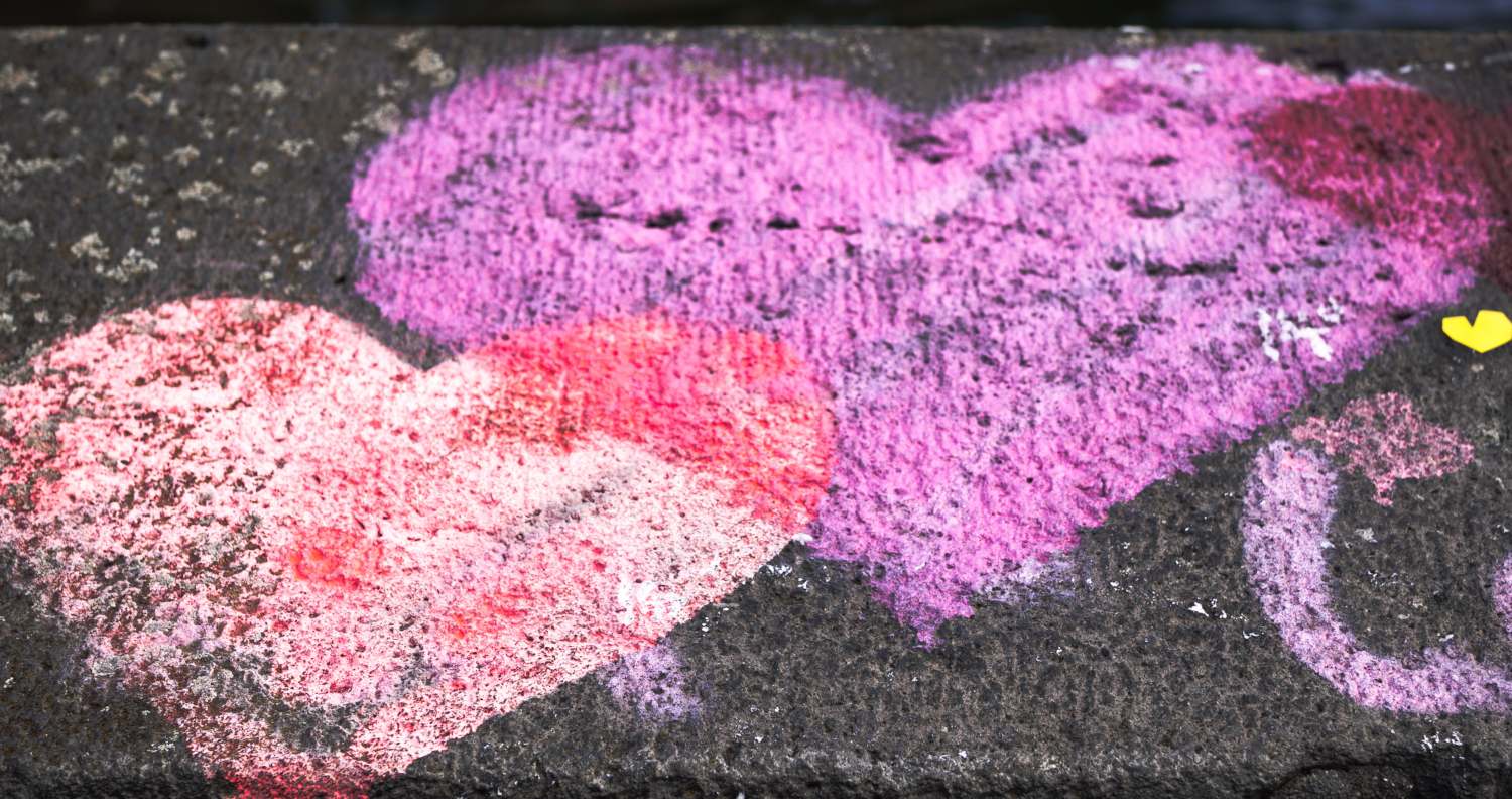 Zwei rosa Herzen, die mit Kreide auf die Straße gemalt sind.