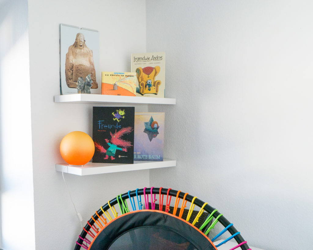 Einblick in einen Beratungsraum, in dem ein Bücherregal mit farbenfrohen Büchern sowie ein sogenanntes Bellicon Trampolin zu sehen ist.