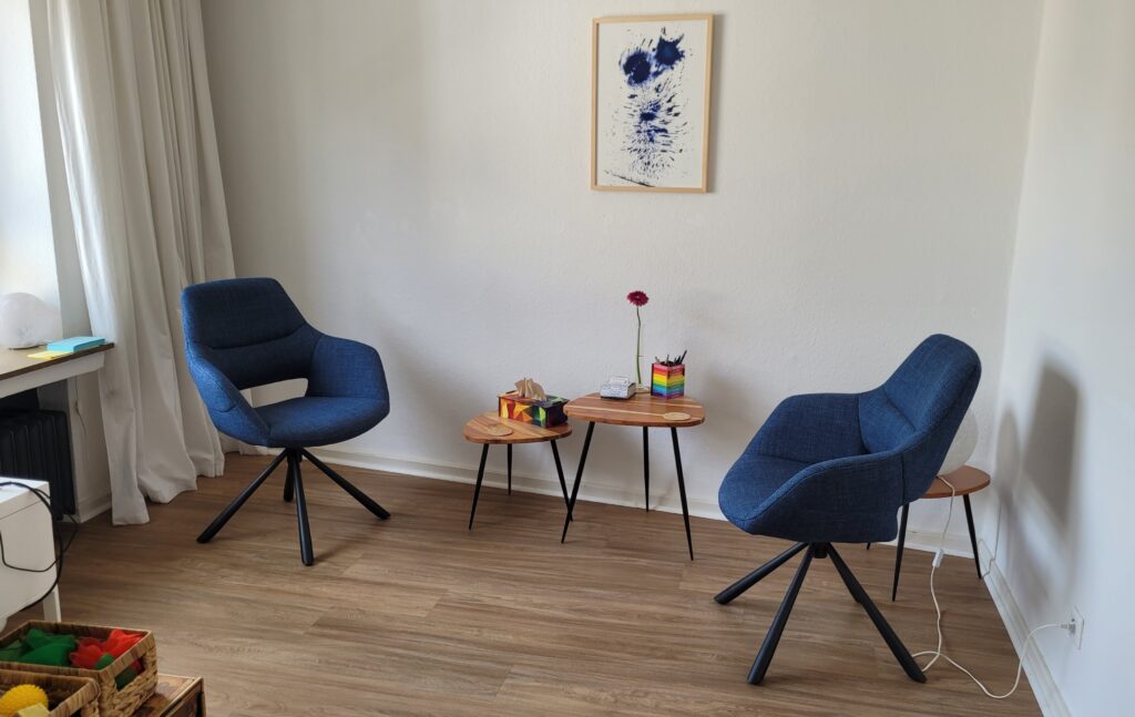 Ein Therapieraum in dem zwei Stühle sich gegenüberstehen. Zwischen ihnen zwei kleine Tische.