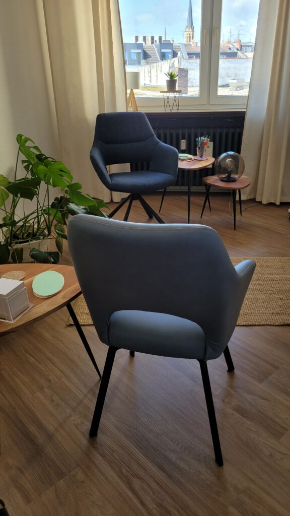 Ein Therapieraum. Zwei verschiedene Stühle stehen sich gegenüber. Neben ihnen stehen kleine Tische, auf denen Material für die Sitzungen bereitstehen.